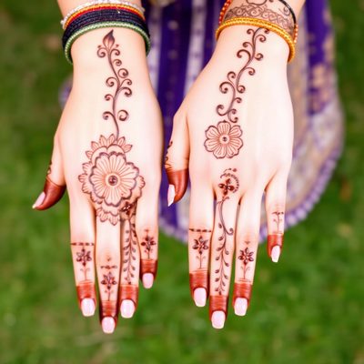 Party mehendi artist applying a simple Arabic design on a guest's hands at home